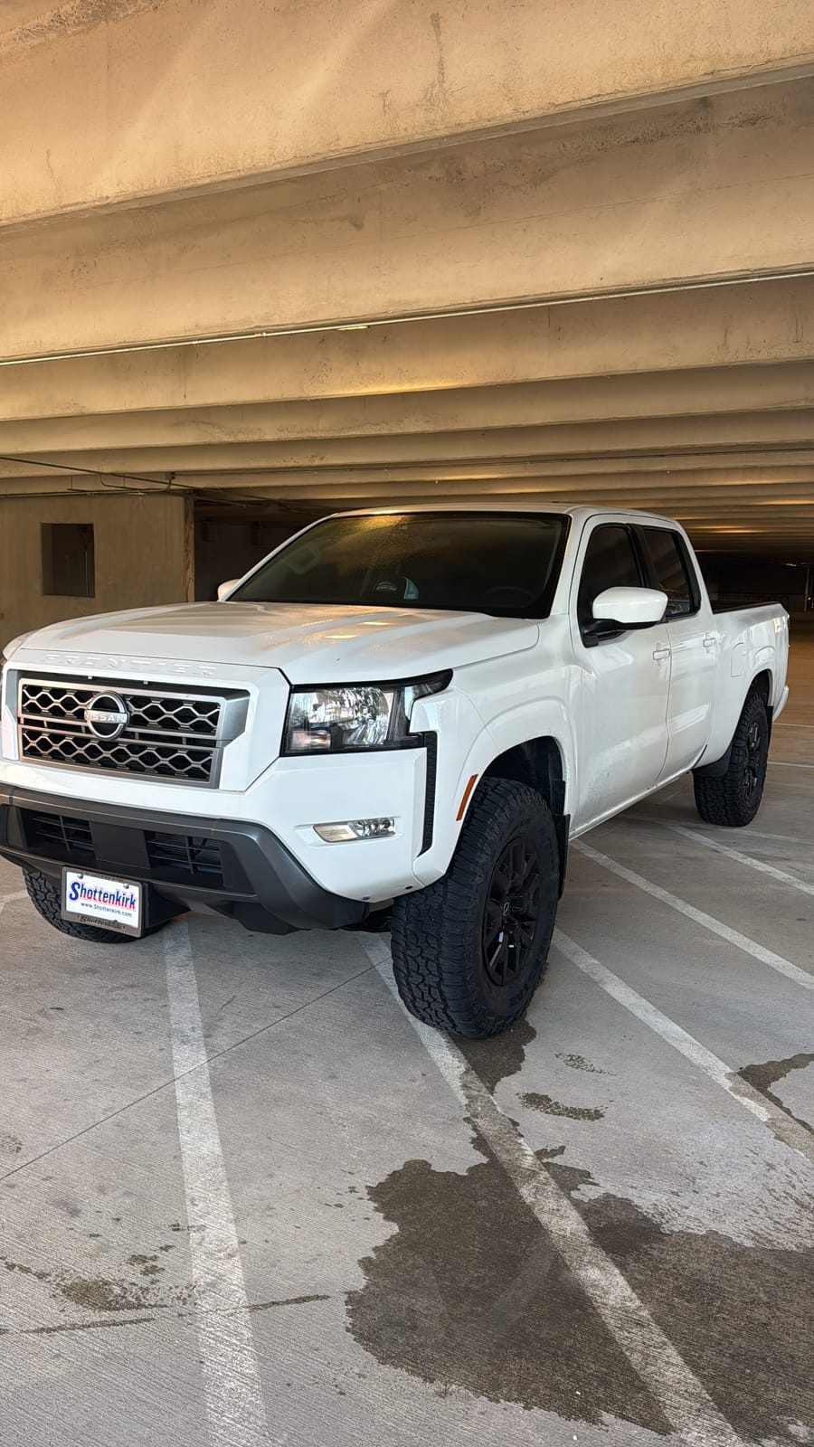 White Nissan Frontier crew-cab pickup with dark tinted front windows in a parking garage
